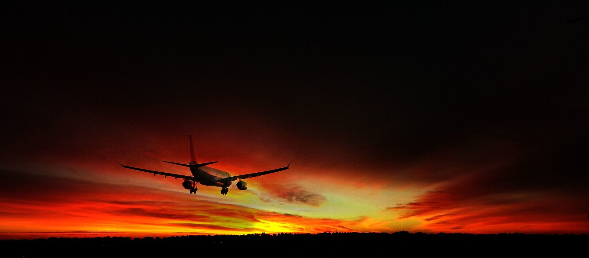 An EgyptAir airliner silhouetted against a red sunset sky on final approach to Cairo International Airport