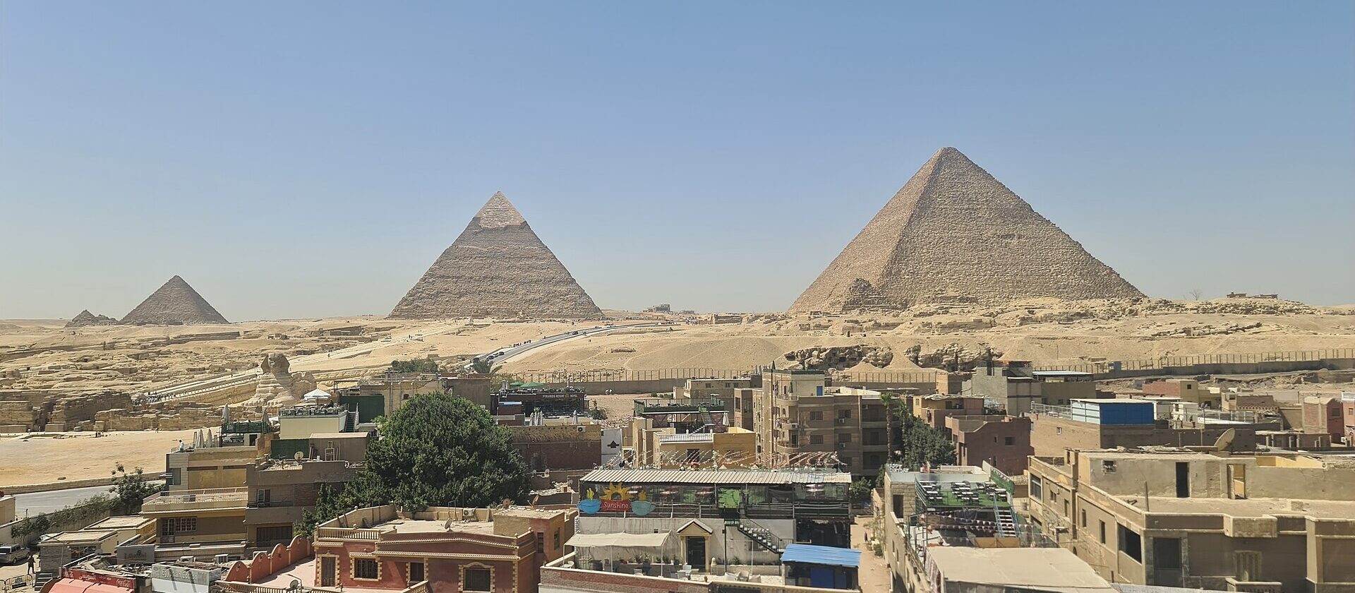 The three main pyramids of Giza and the Sphinx seen above the rooftops and cafés of Nazlet el-Samman on a clear day