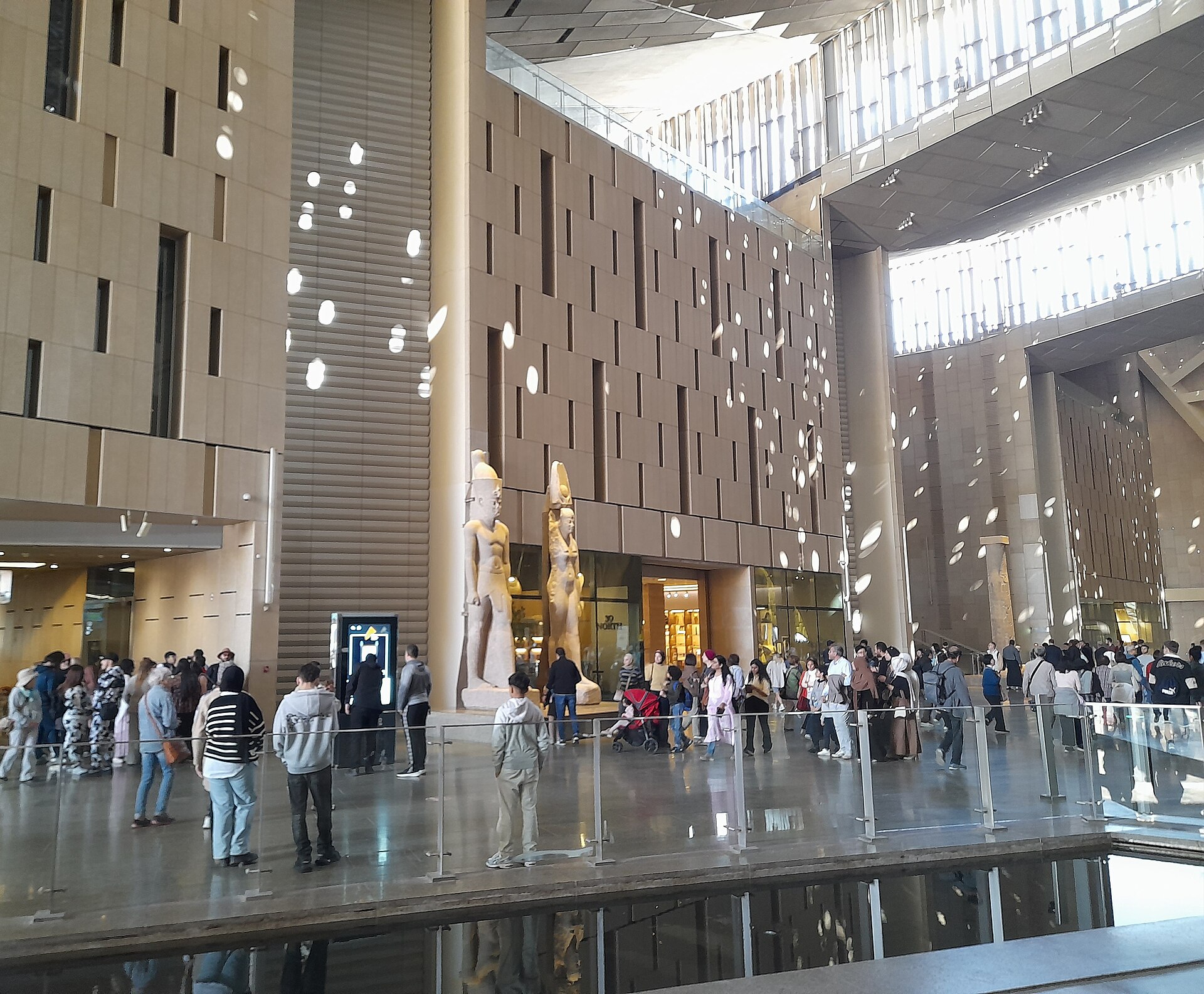 Grand Egyptian Museum with Kids: Family Visit Guide 3 Crowds including a family with a red pushchair in the atrium of the Grand Egyptian Museum beside colossal royal statues