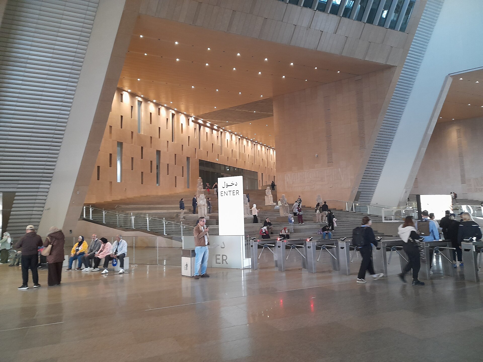 Visitors passing through the entry turnstiles at the Grand Egyptian Museum below a bilingual Arabic and English ENTER sign
