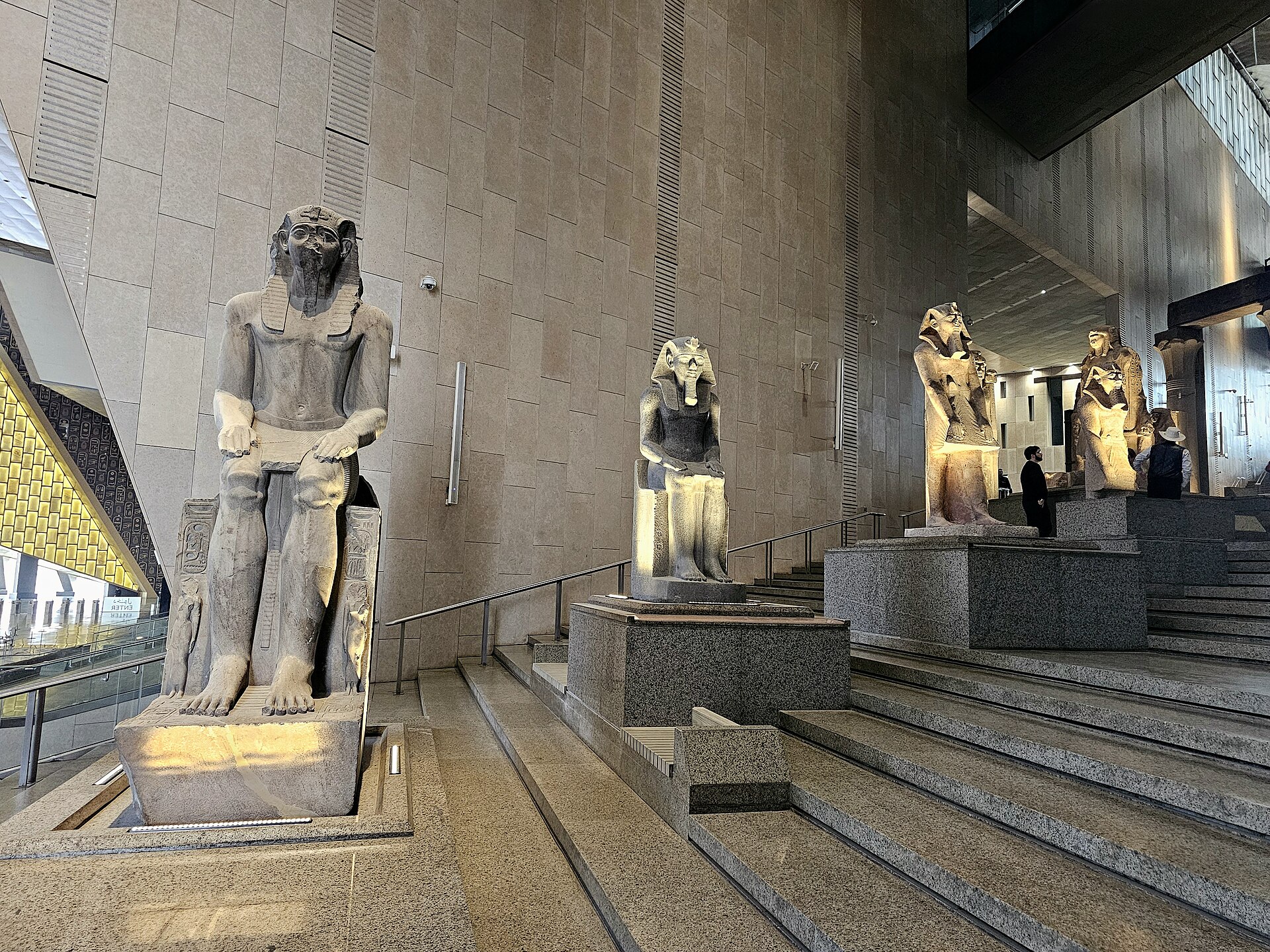 Seated colossal pharaonic statues lining the Grand Staircase of the Grand Egyptian Museum as it climbs between levels