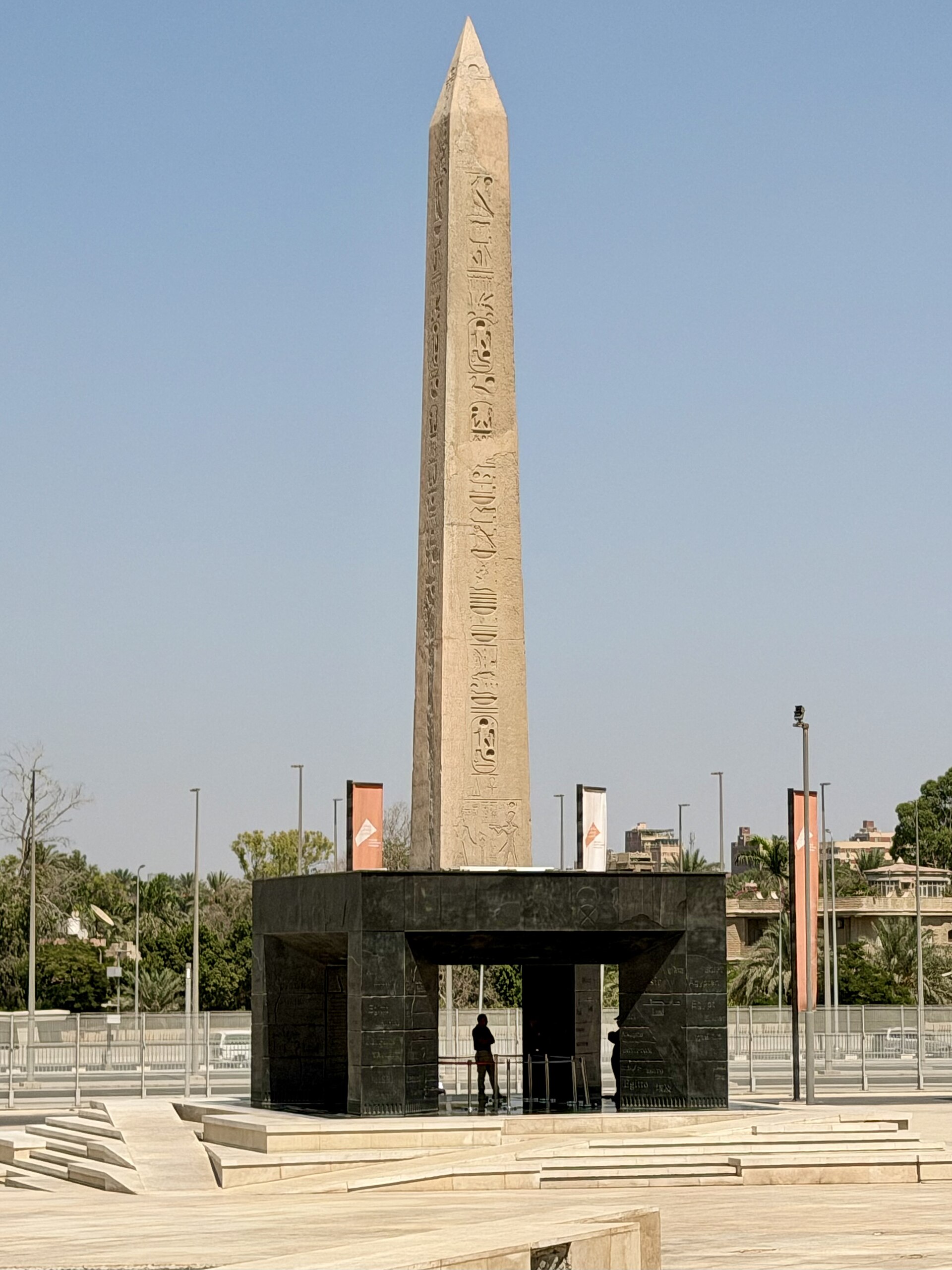 The hanging obelisk mounted above a dark stone base on the entrance plaza of the Grand Egyptian Museum