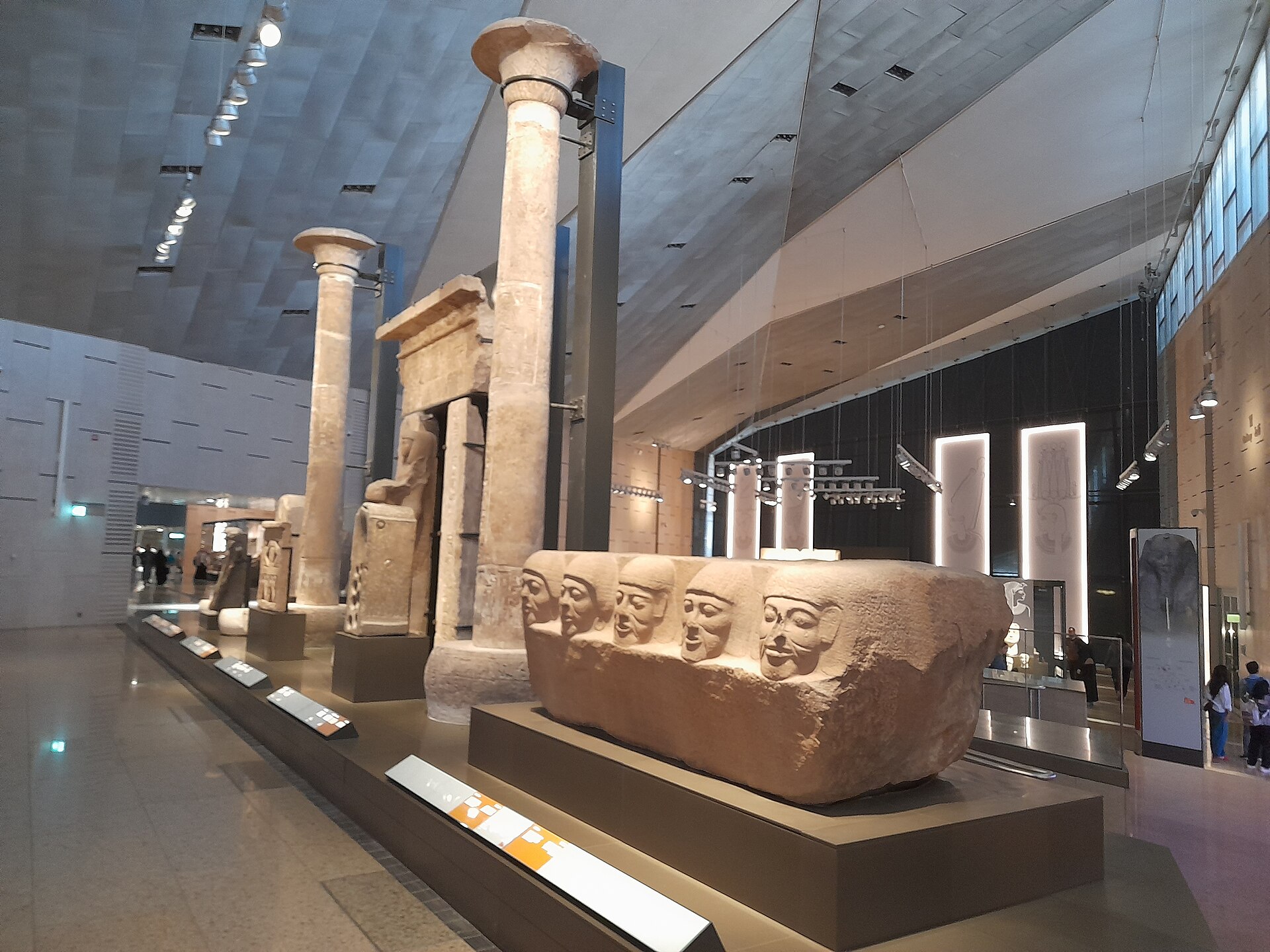 Grand Egyptian Museum vs Egyptian Museum Tahrir: Which Should You Visit? 2 Main galleries at the Grand Egyptian Museum with temple columns, a carved block of five heads and modern interpretive panels