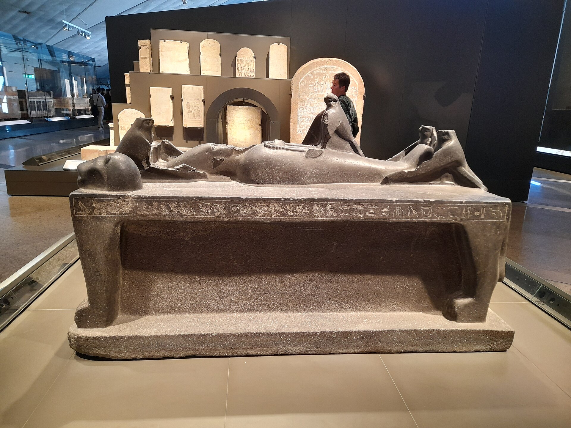 A granite funerary couch with falcon figures displayed in a near-empty gallery at the Grand Egyptian Museum