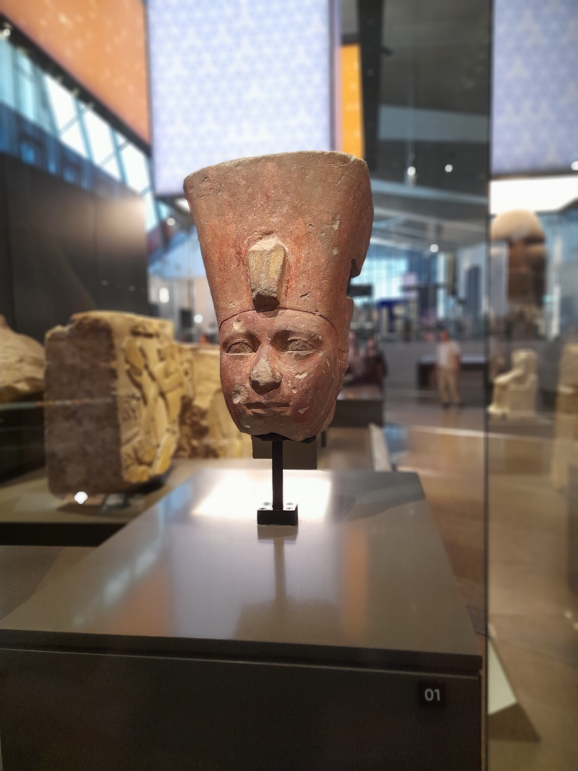 A limestone head of a pharaoh in a glass case with the museum galleries and glazed facade visible behind