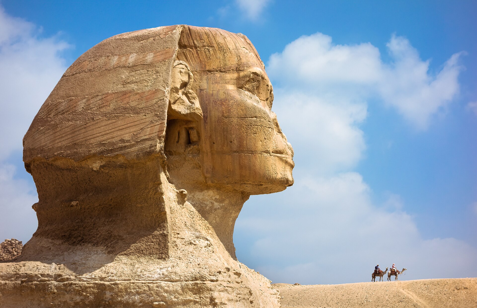 One Day in Cairo: The Perfect 24-Hour Itinerary 2 The Great Sphinx of Giza in profile against a blue sky with two camel riders on the ridge behind