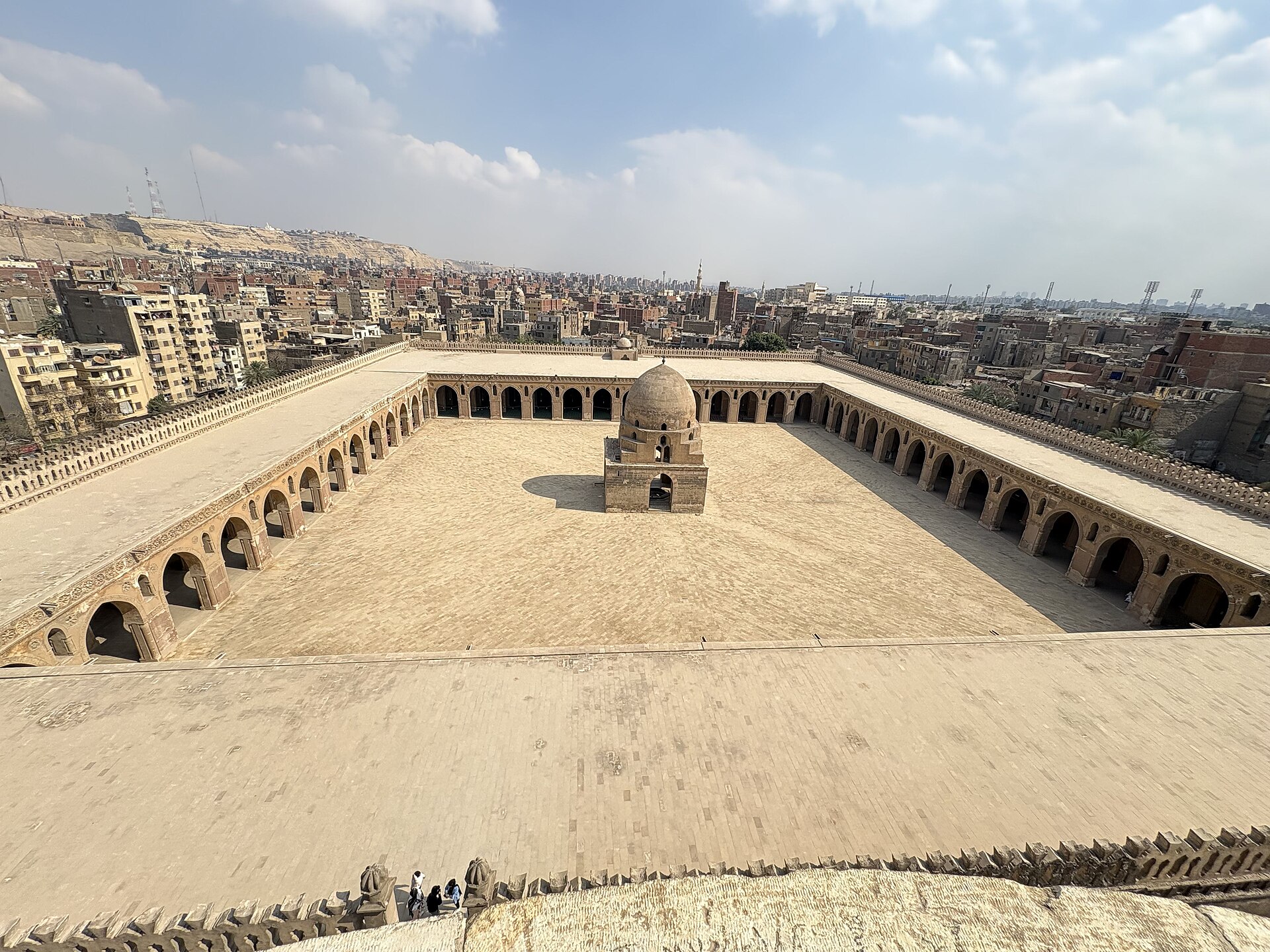 The vast courtyard of the Mosque of Ibn Tulun in Cairo seen from above, with the city beyond