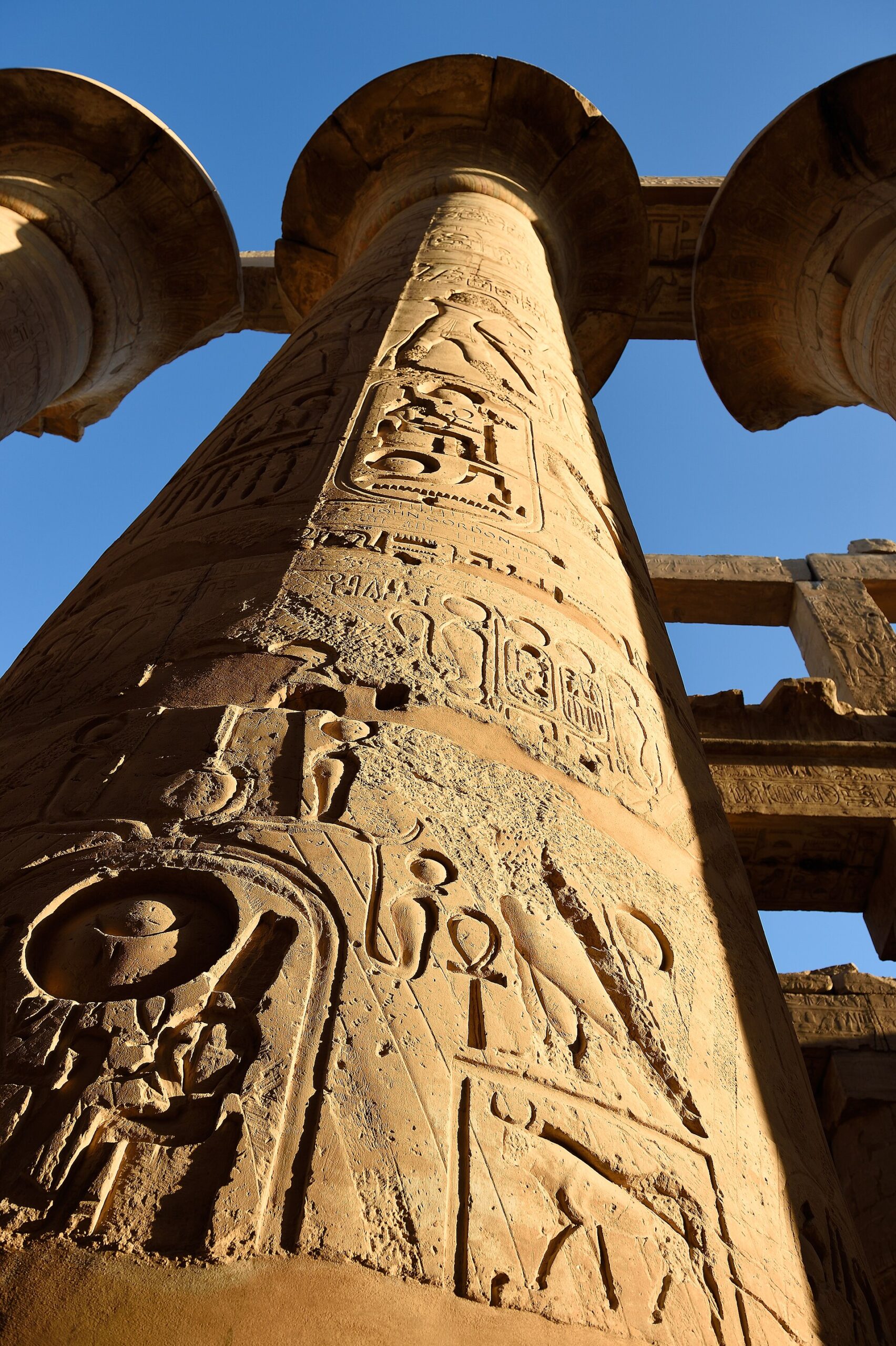 Carved sandstone column in the Great Hypostyle Hall at Karnak Temple in Luxor against a blue sky