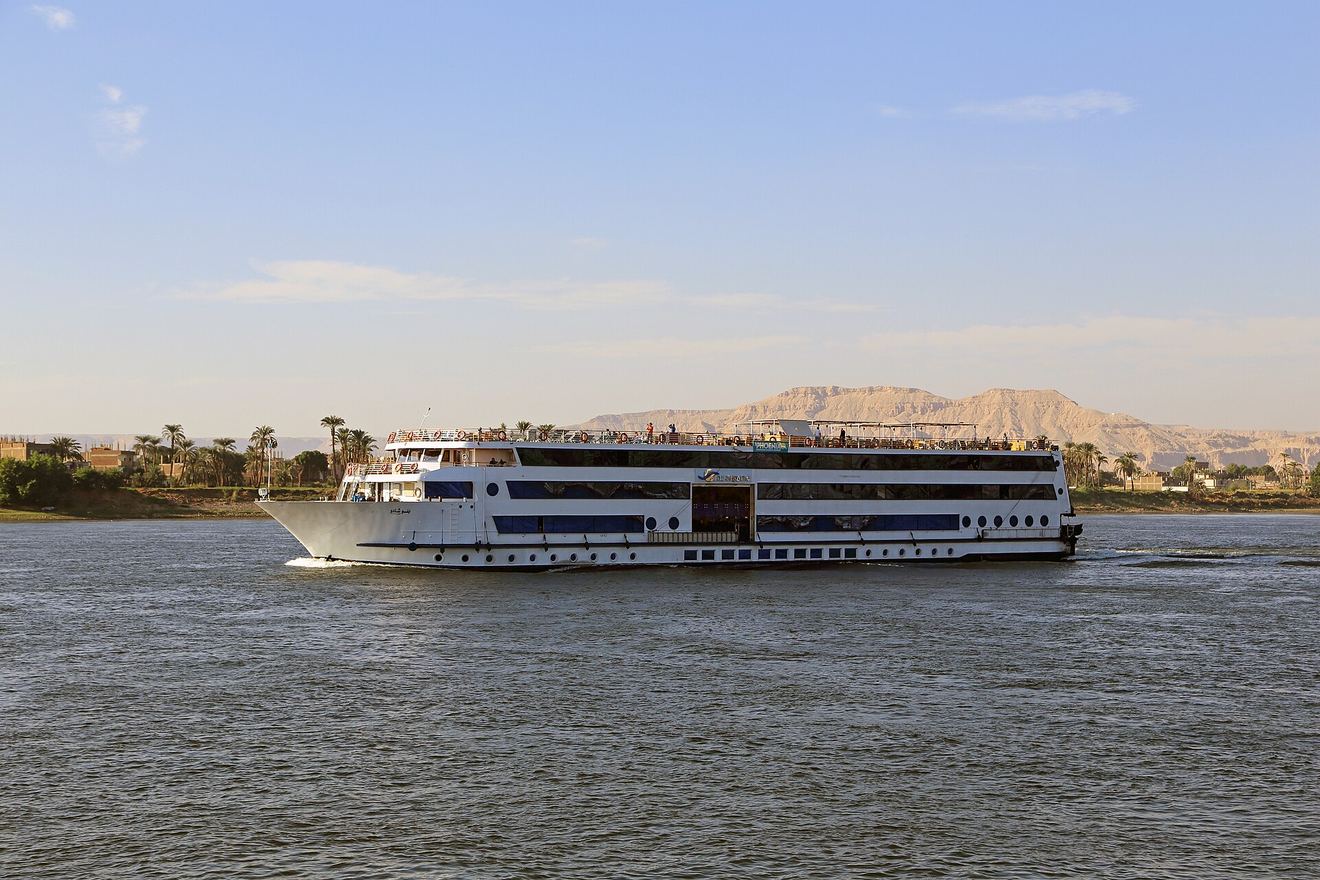A white Nile cruise ship under way on the river with the Theban hills behind