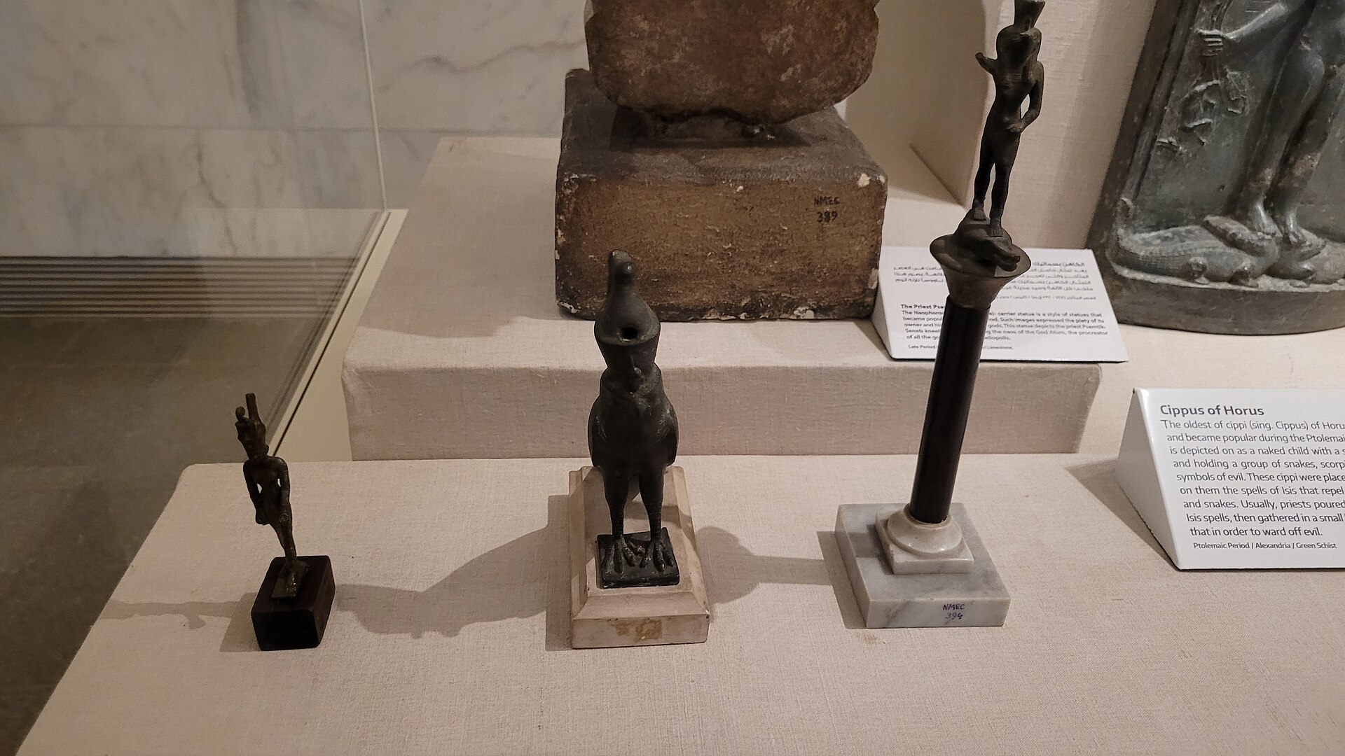 National Museum of Egyptian Civilization and the Royal Mummies 3 Bronze figurines including a falcon and a cippus of Horus displayed in a case at the National Museum of Egyptian Civilization with bilingual labels