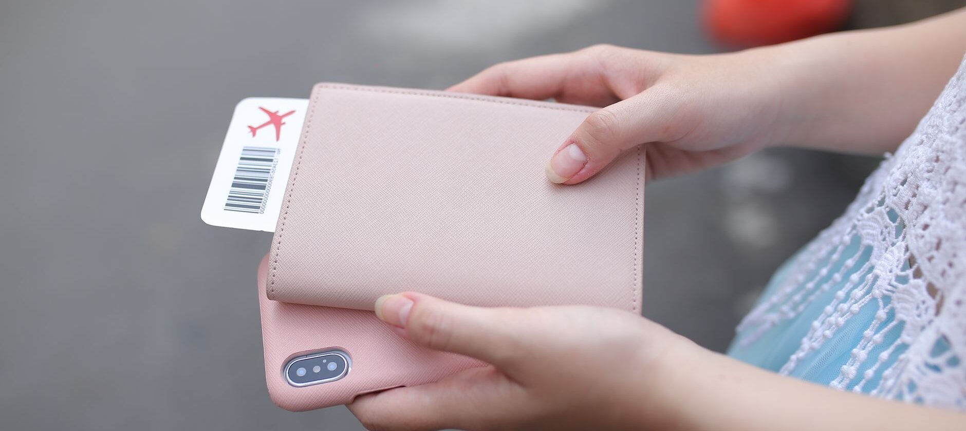 Hands holding a passport in a pink cover with a boarding pass tucked inside and a smartphone underneath