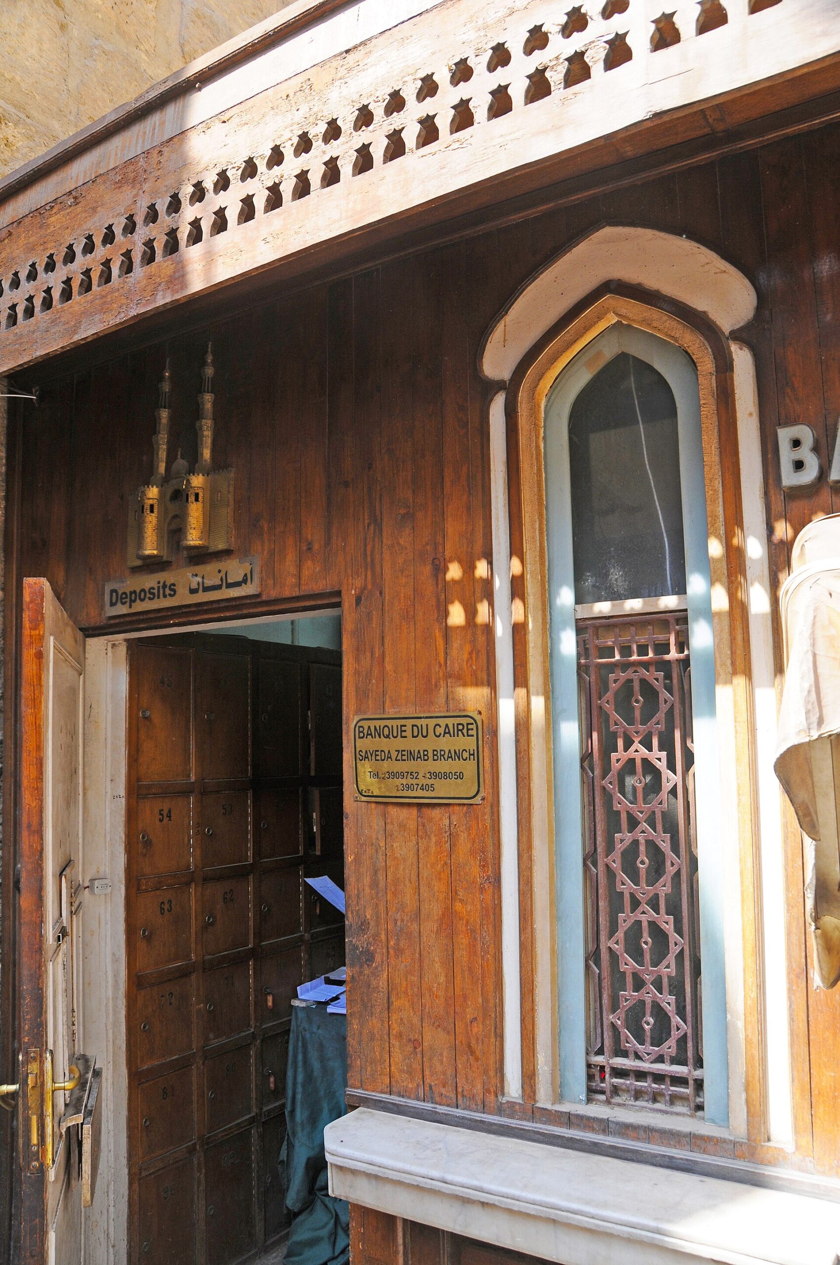 The carved wooden entrance of a Banque du Caire branch in the Sayeda Zeinab district of Cairo, with a brass plaque beside the door