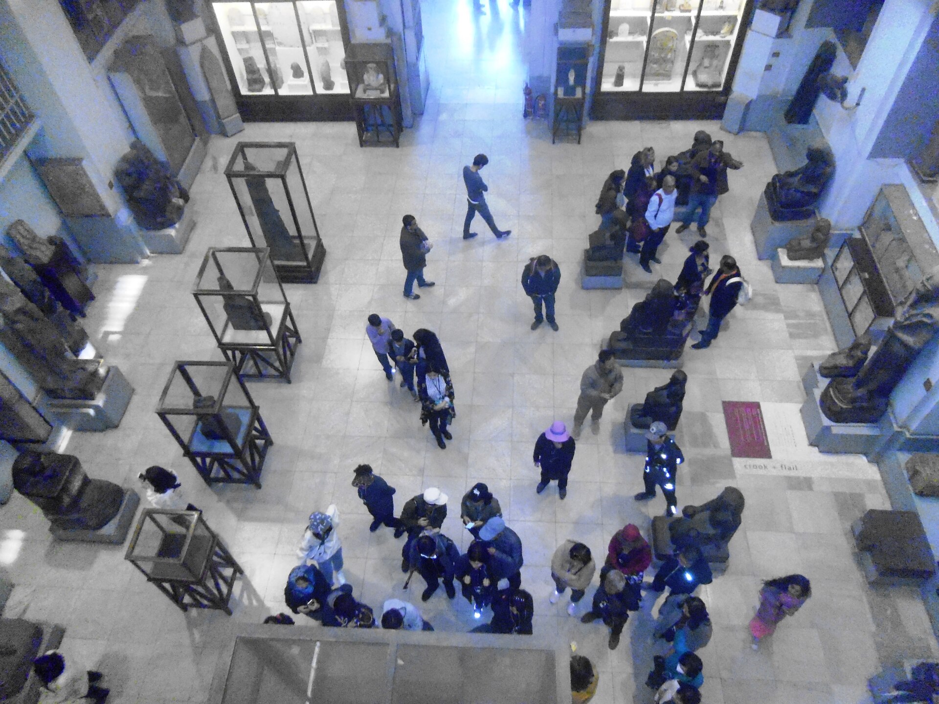 Visitors moving between statues and glass display cases in a large hall of the Egyptian Museum in Cairo, seen from the gallery above