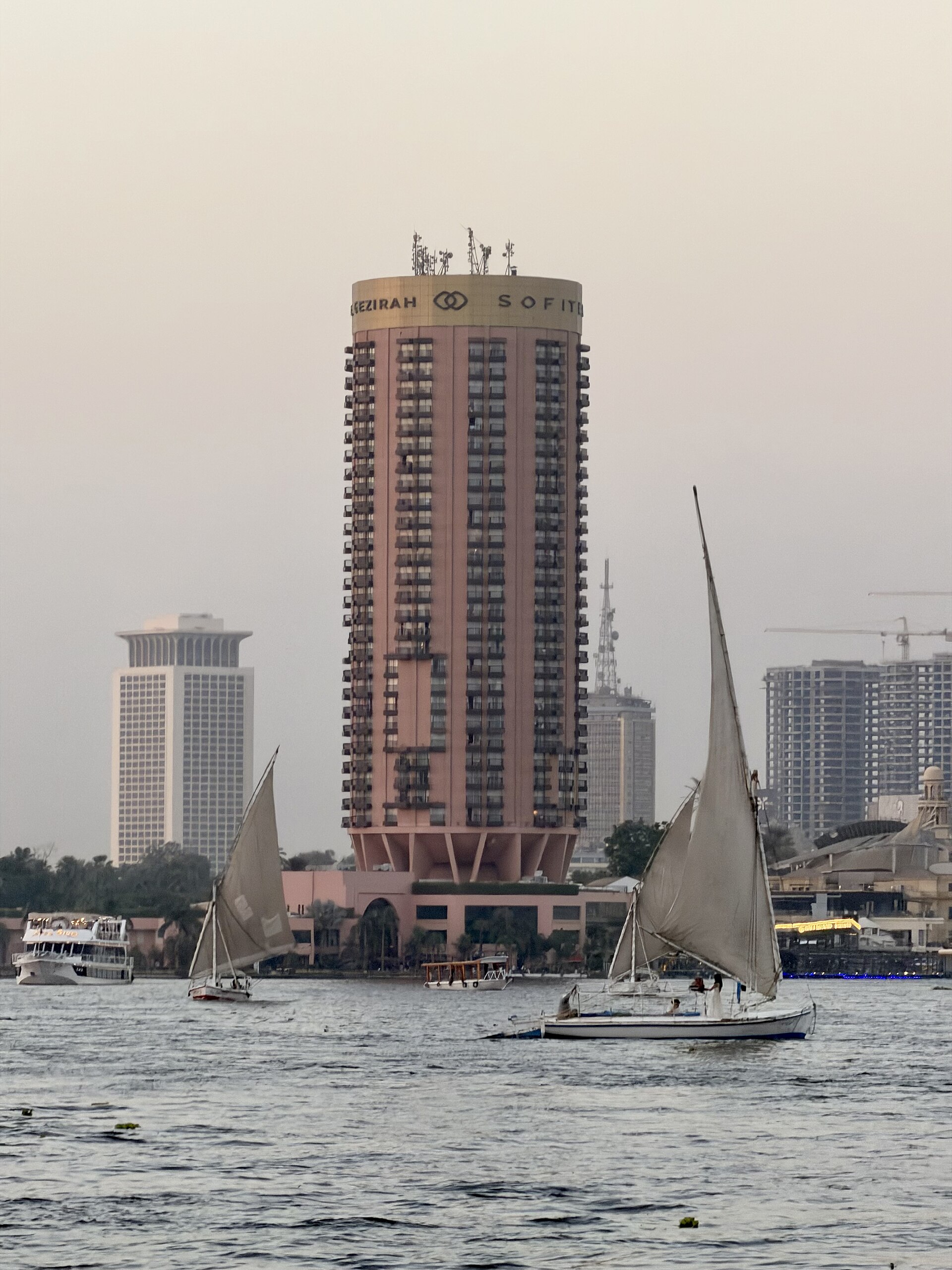 Cairo Tours and Tickets: How to Choose and Book 3 Two white-sailed feluccas on the Nile in Cairo, with a tall round hotel tower and riverside buildings behind