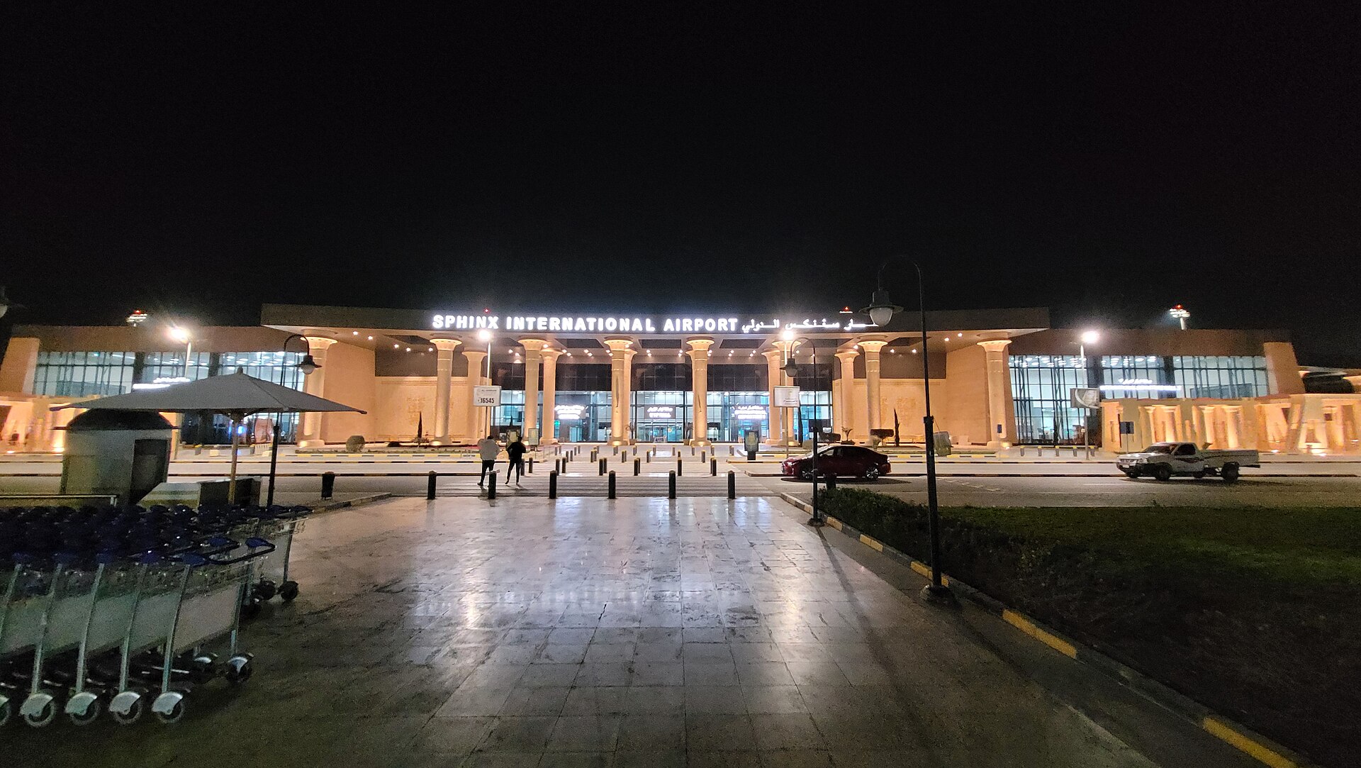 Sphinx International Airport and Cairo's Other Airports 2 The forecourt of Sphinx International Airport at night, with luggage trolleys lined up and the lit, columned terminal behind