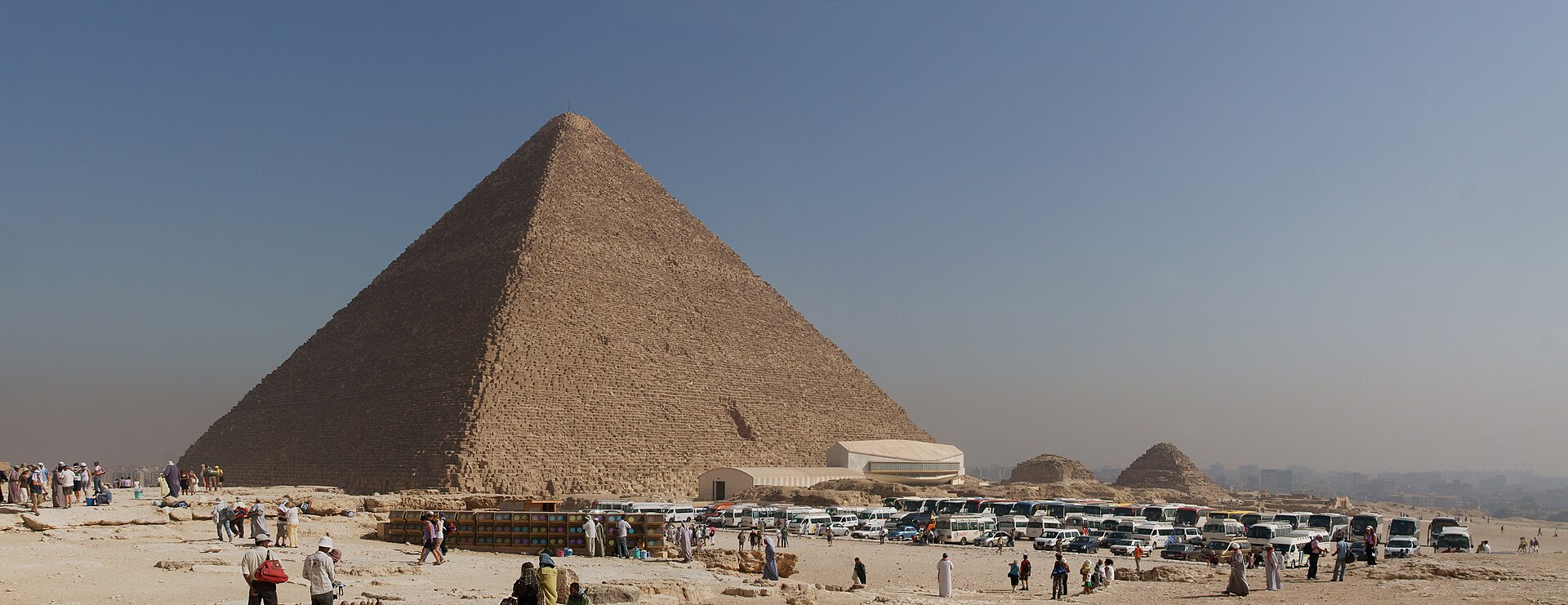 Rows of tour buses and visitors on the Giza plateau below the Great Pyramid on a hazy day